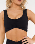 close up of young woman wearing black low scoop activewear crop.