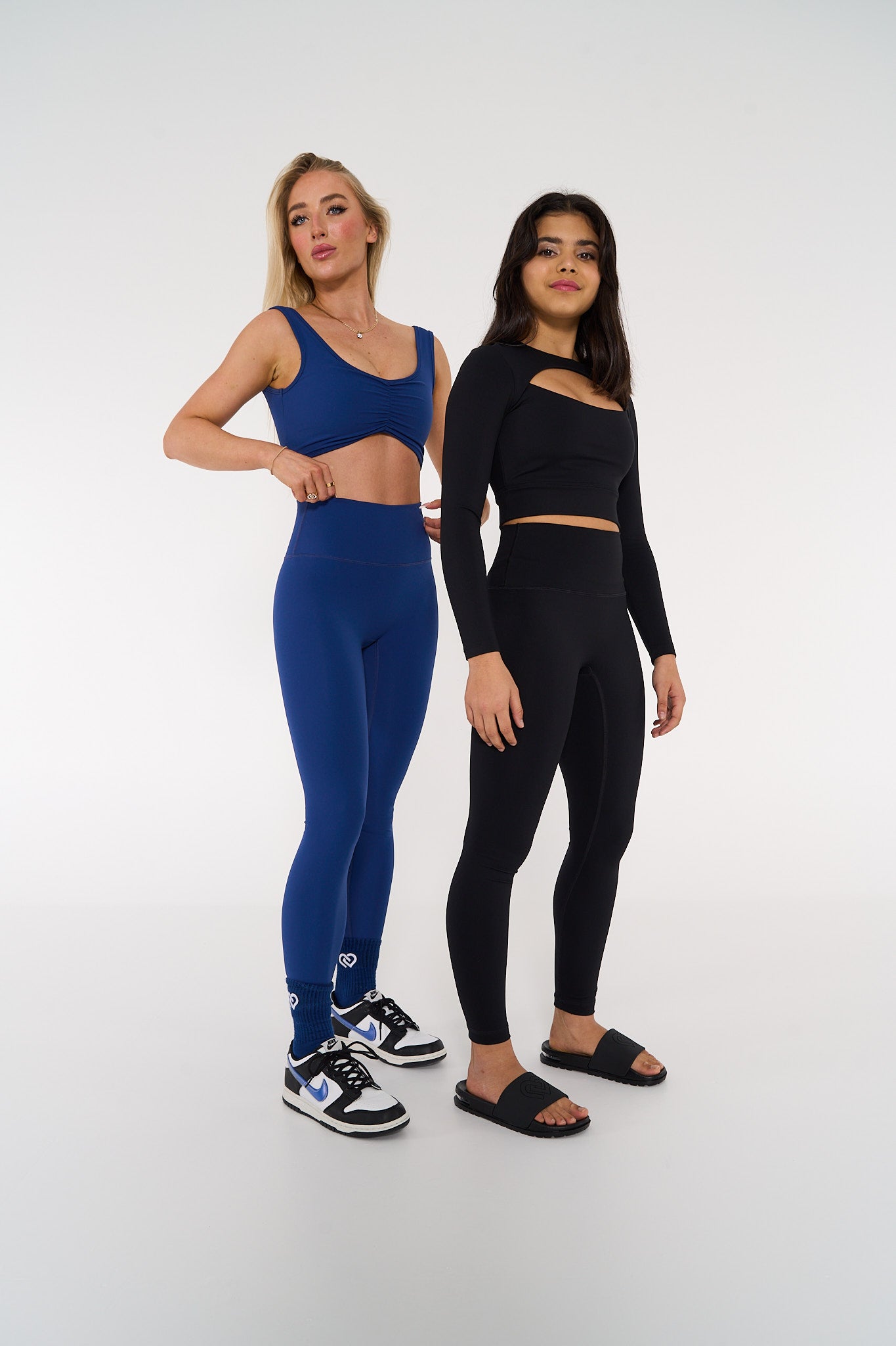 young woman wearing black long sleeve cut out activewear crop &amp; another young woman wearing navy activewear.