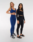 young woman wearing black long sleeve cut out activewear crop & another young woman wearing navy activewear.