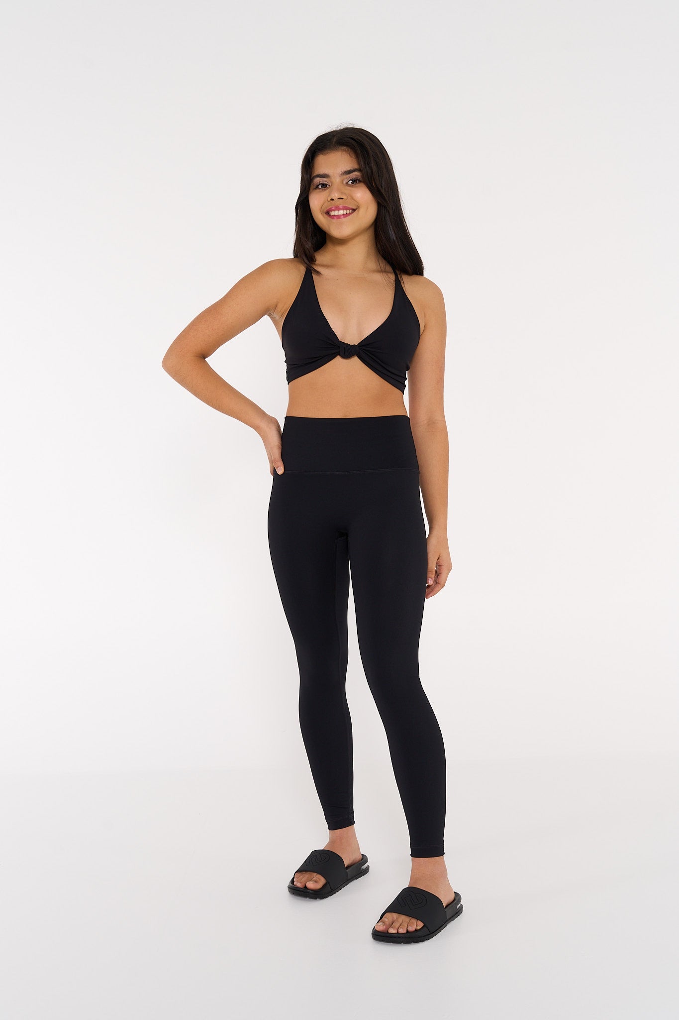 young woman wearing black twist knot activewear crop with black high waisted tights