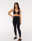 young woman wearing black twist knot activewear crop with black high waisted tights