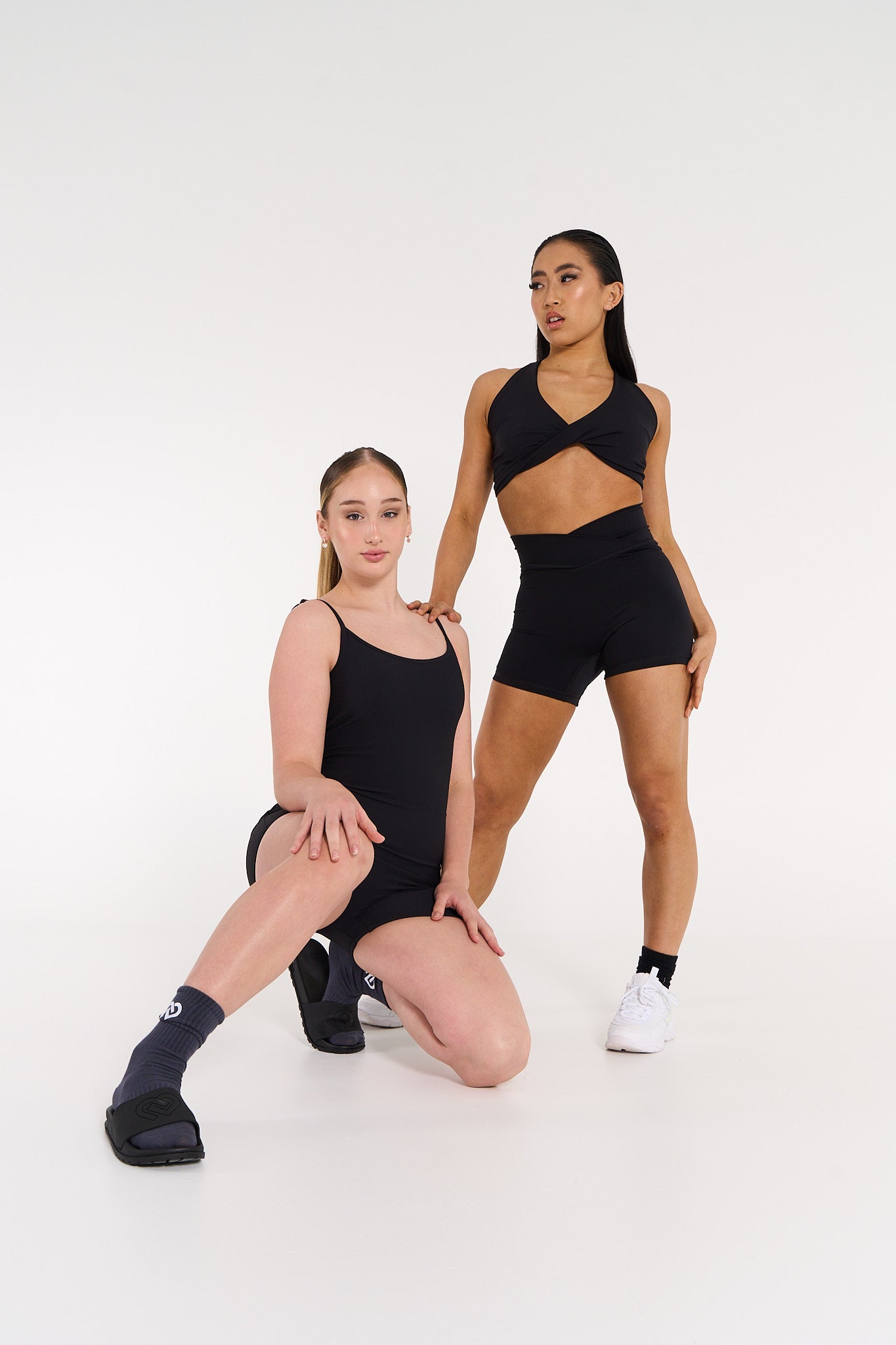 young woman wearing high waisted black v style active shorts and young woman wearing ribbed black bodysuit