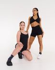 young woman wearing high waisted black v style active shorts and young woman wearing ribbed black bodysuit